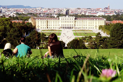 Student sits on the lawn in front of a large European-style building.